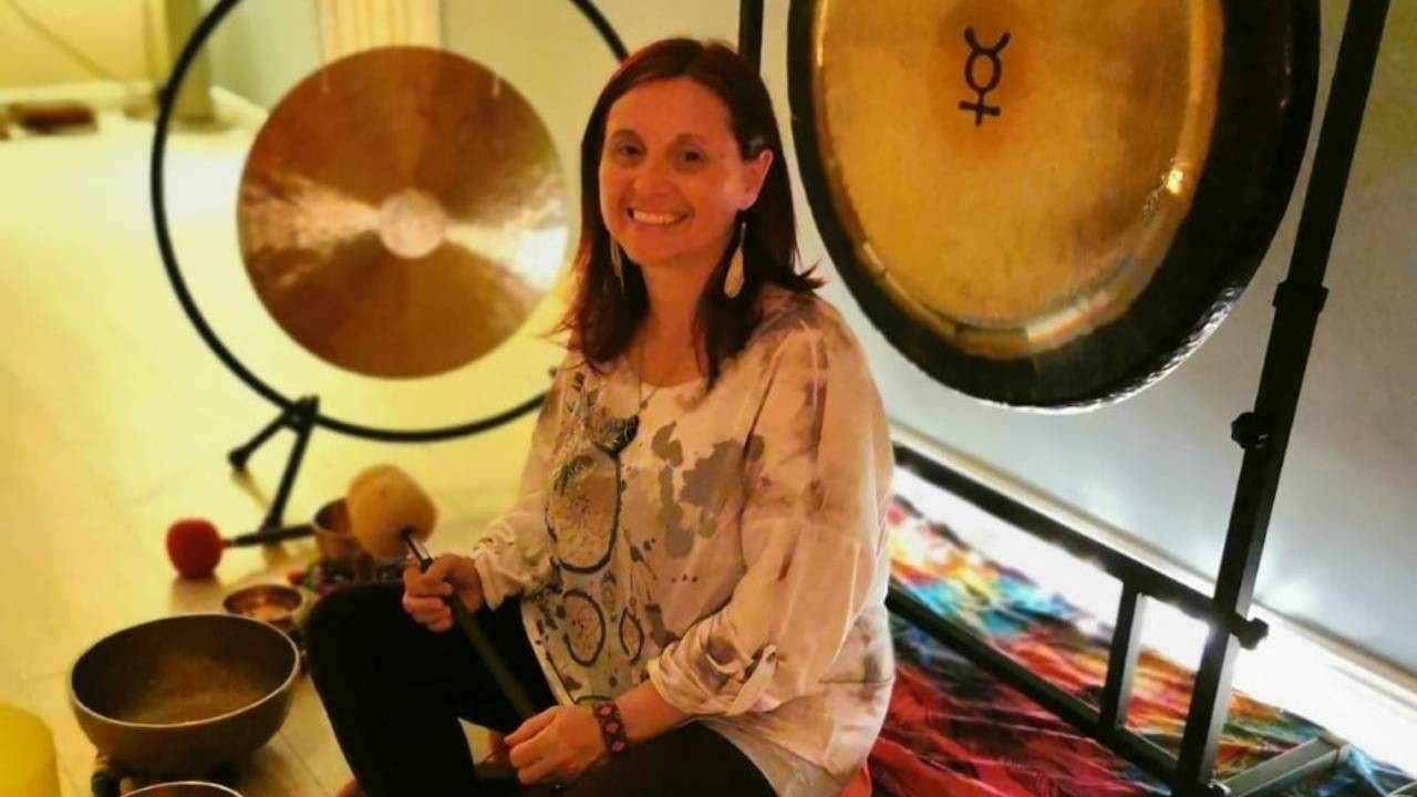 Woman with a large smile surrounded by standing gongs and sound healing instruments