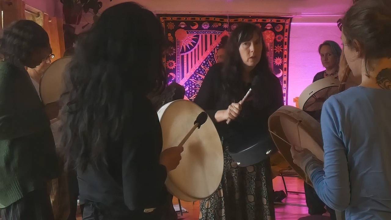 Women beating drums in a pink lighted room