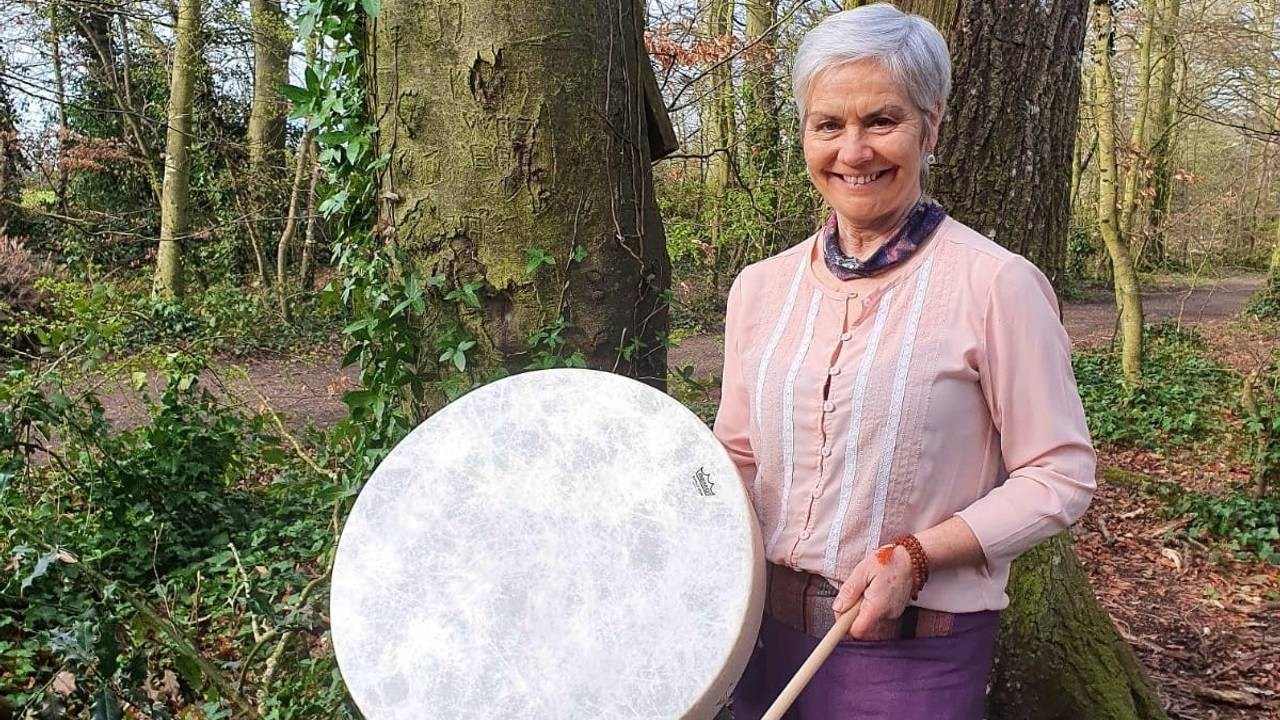 White headed short hair woman holding a drum and a beater in the forest