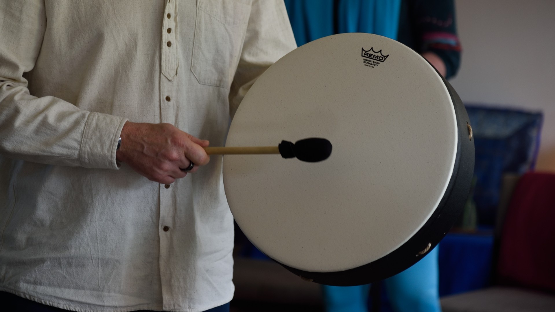 Man in a white shirt holding a drum and beating it with a beater