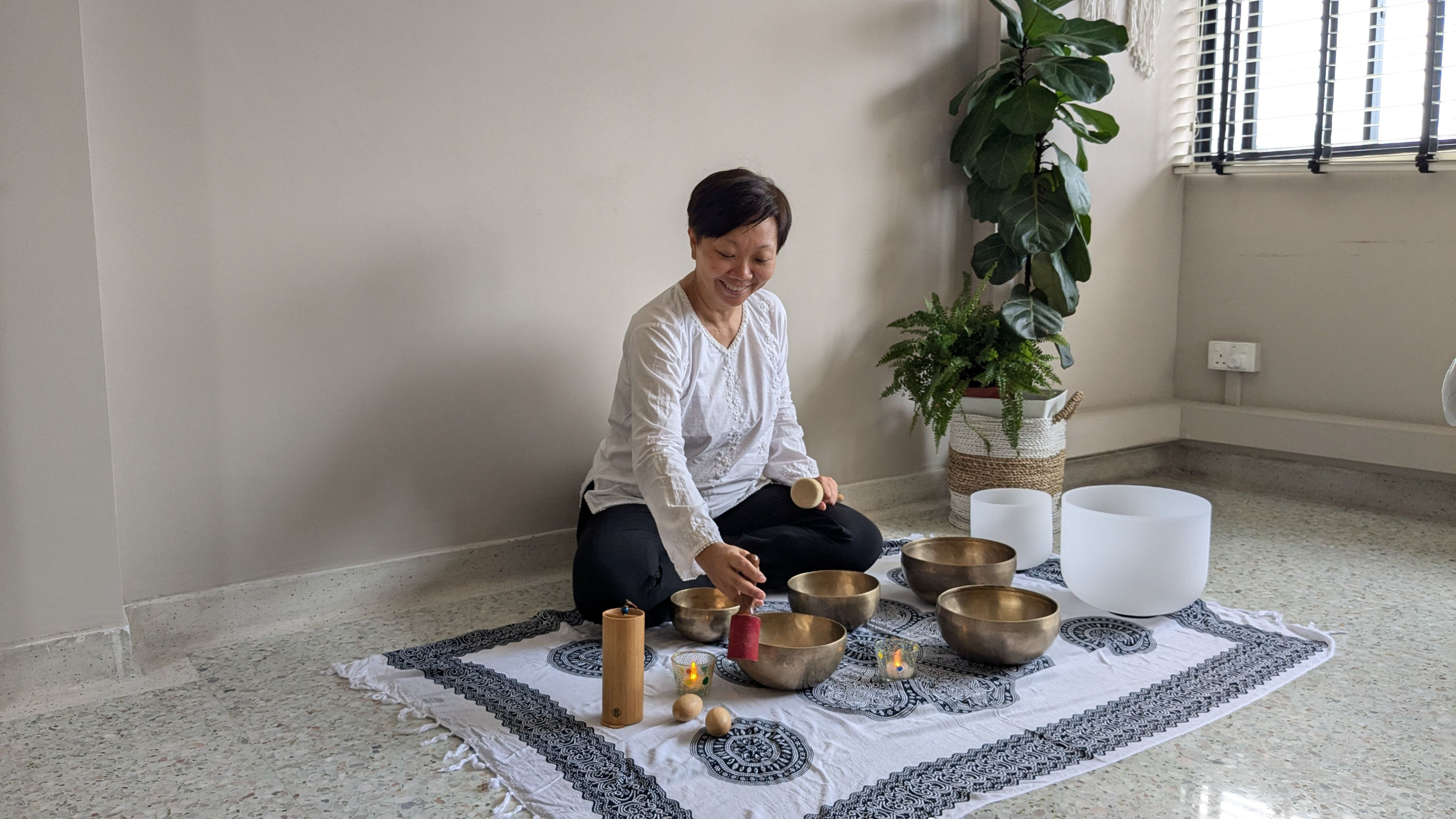 Woman playing a tibetan singing bowl on a white rug indoors