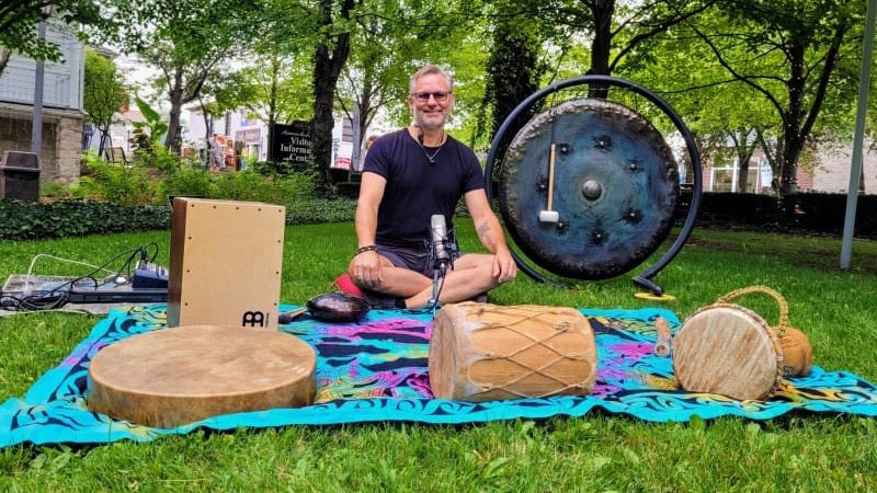 Man with glasses on the grass, surrounded by sound healing instruments