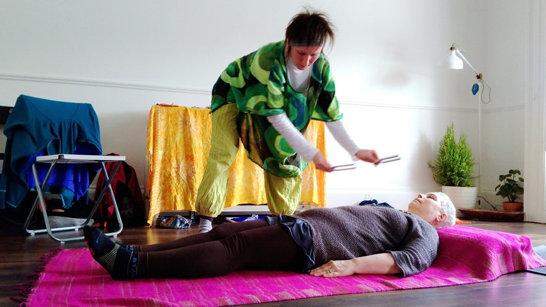 Woman doing sound healing on her client with tuning forks above the body
