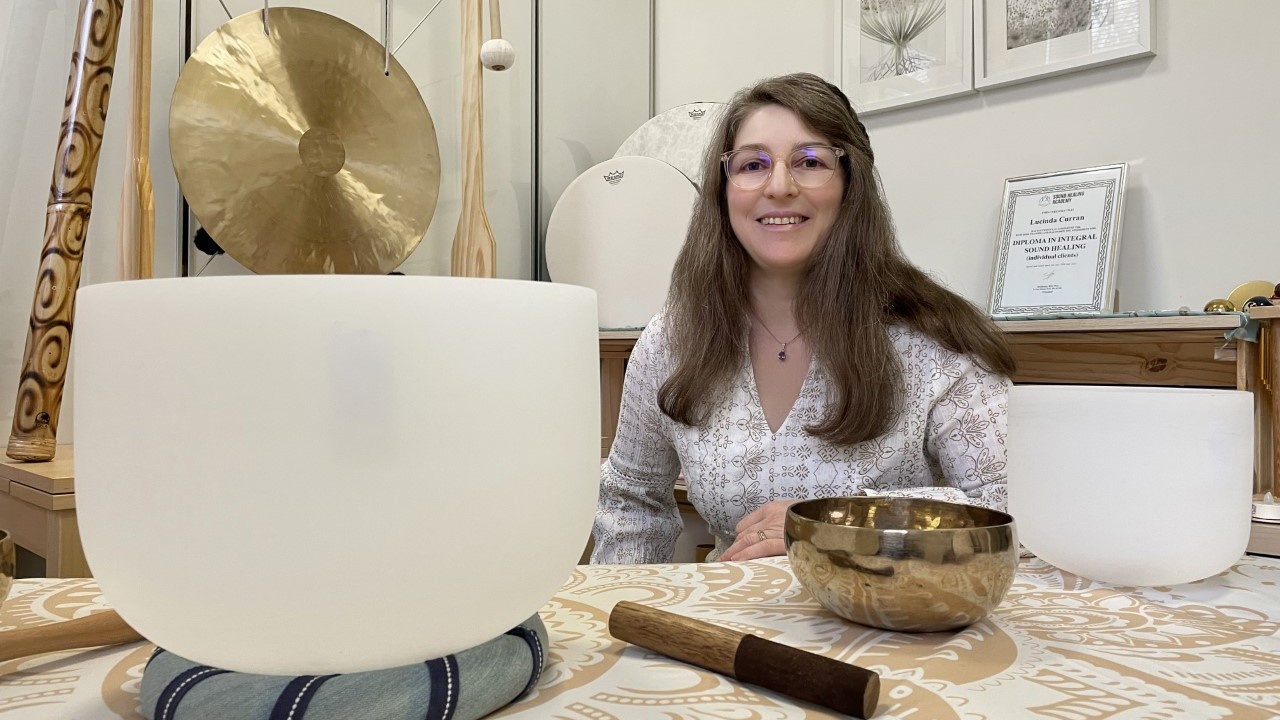 Woman with glasses smiling behind sound healing instruments indoors