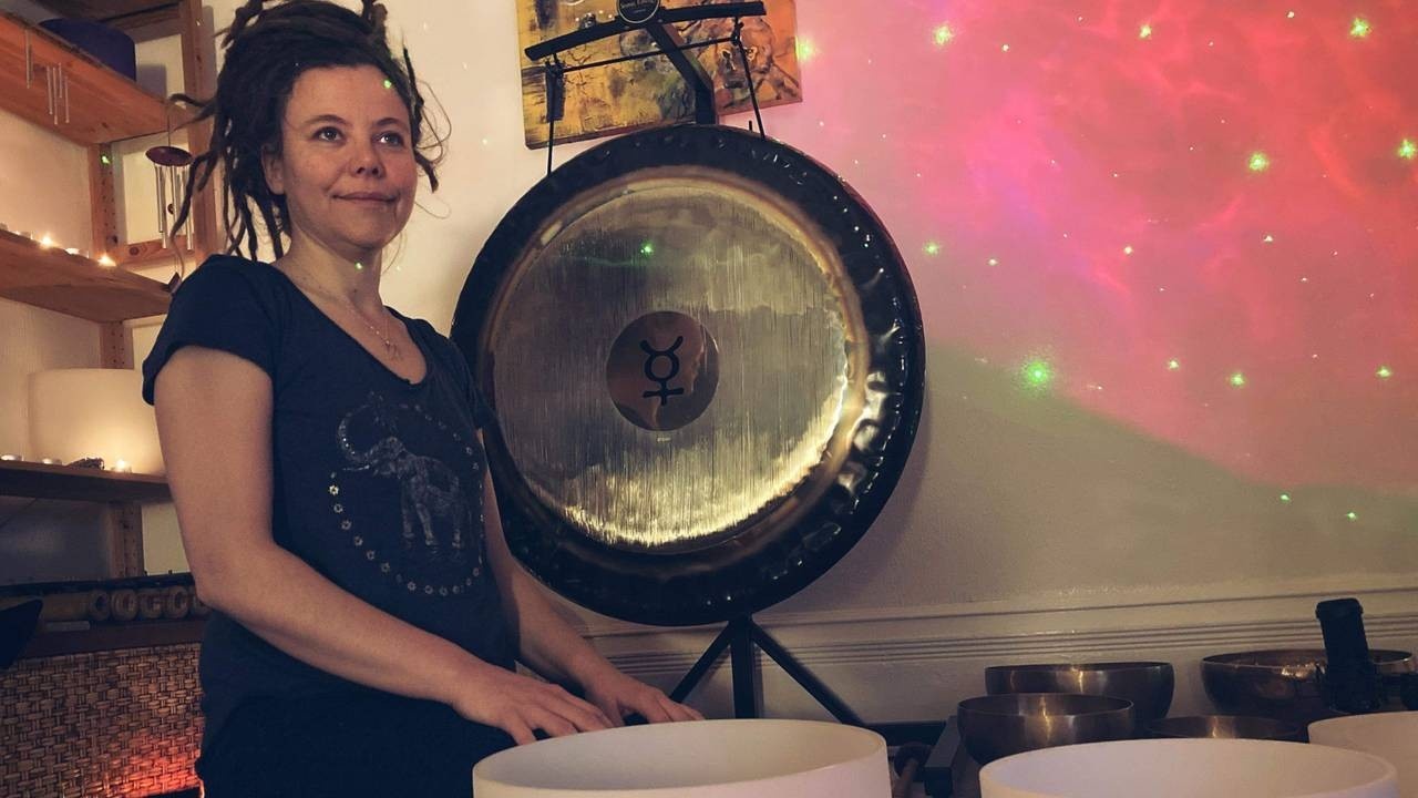 Woman sitting down next to a large gong and crystal singing bowls 