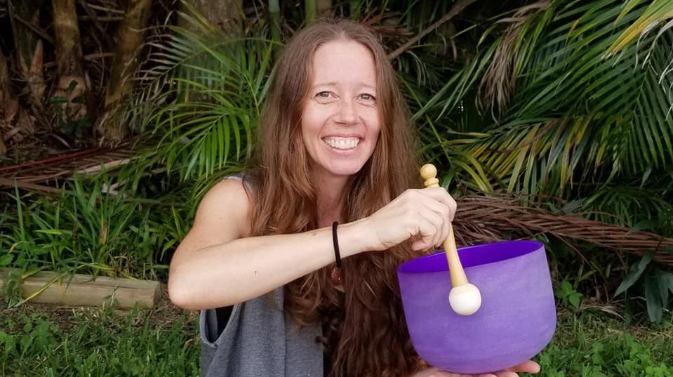 Smiling woman sound healer, playing the rim of a purple crystal singing bowl