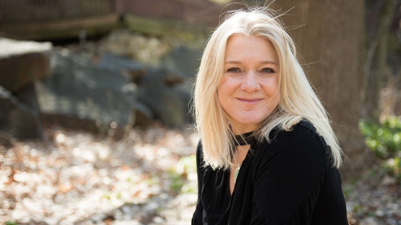 Blonde sound healing practitioner woman smiling in front of a tree