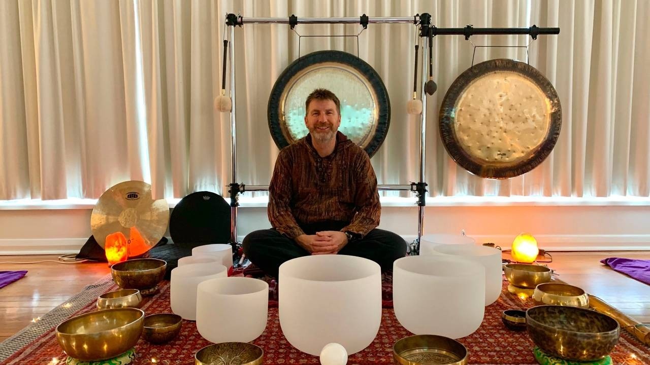 Sound healing practitioner sitting down in the middle of an area with sound healing instruments