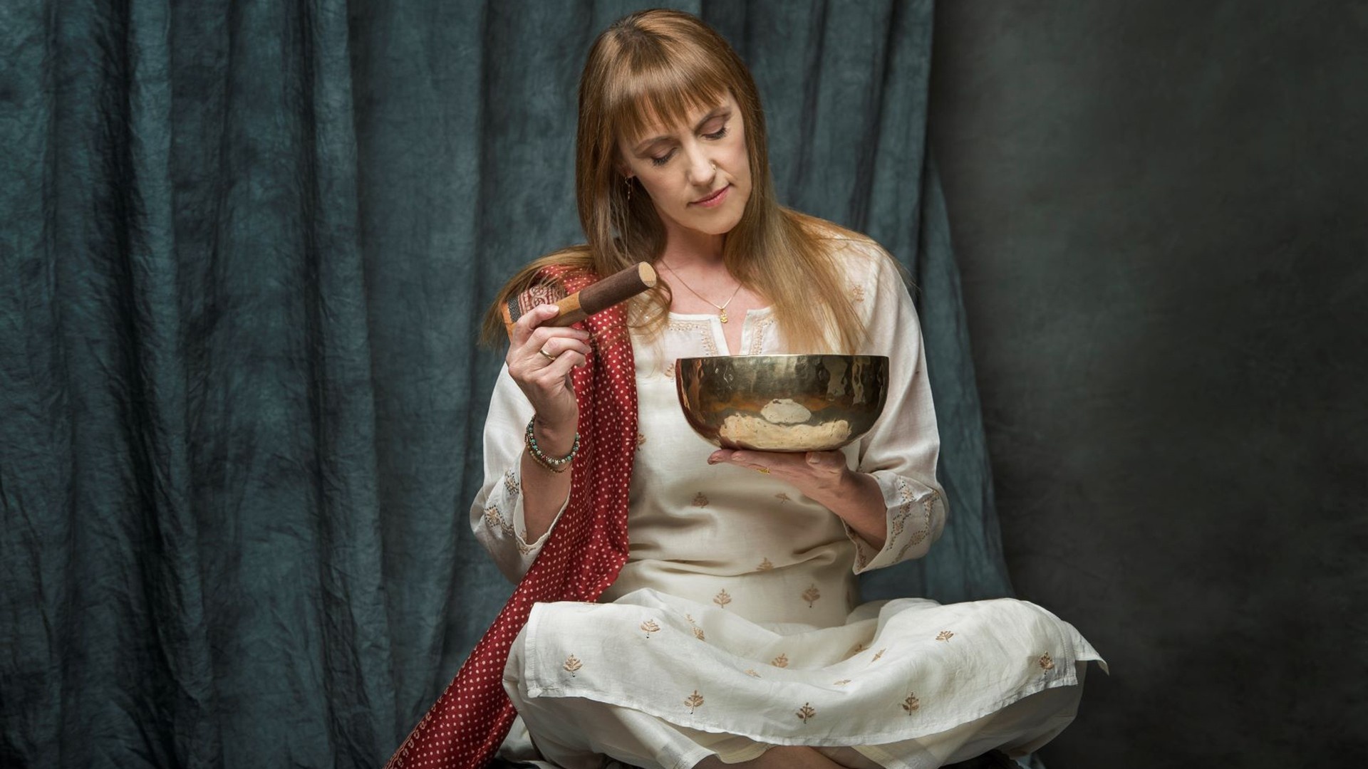 Woman holding a tibetan singing bowl in front of a dark green background