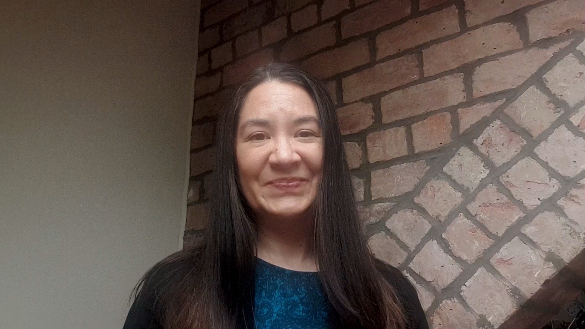 Woman with brown hair in front of a brick wall smiling