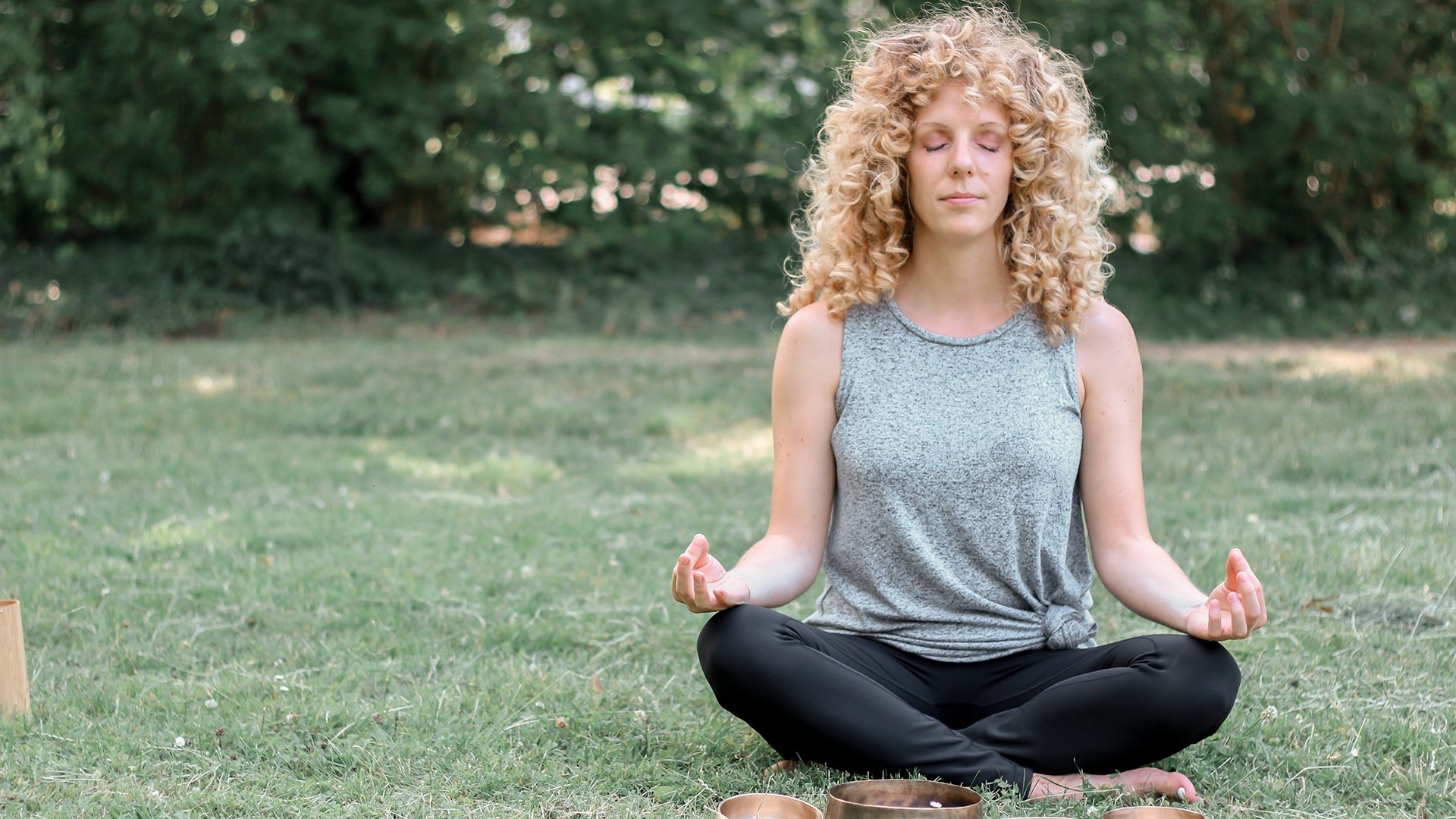 Woman with blonde curly hair meditating on the grass in nature