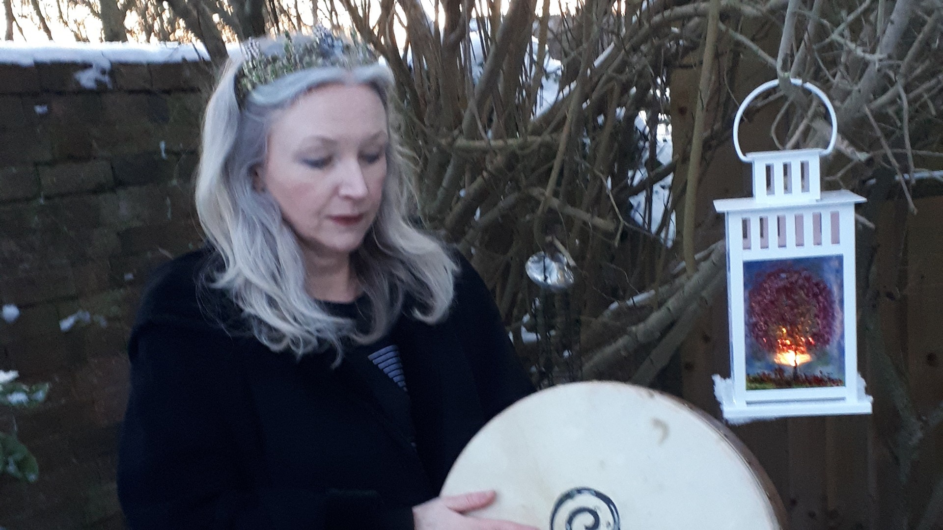 Sound healing practitioner, holding a hand held drum outdoors in the snow