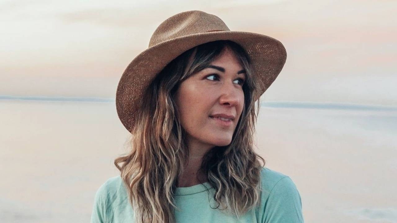 woman smiling and looking on her side, with a hat on and a green shirt