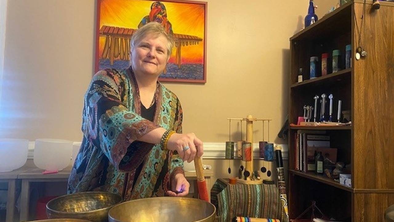 Woman playing a large tibetan singing bowl's rim in a room with other sound healing instruments