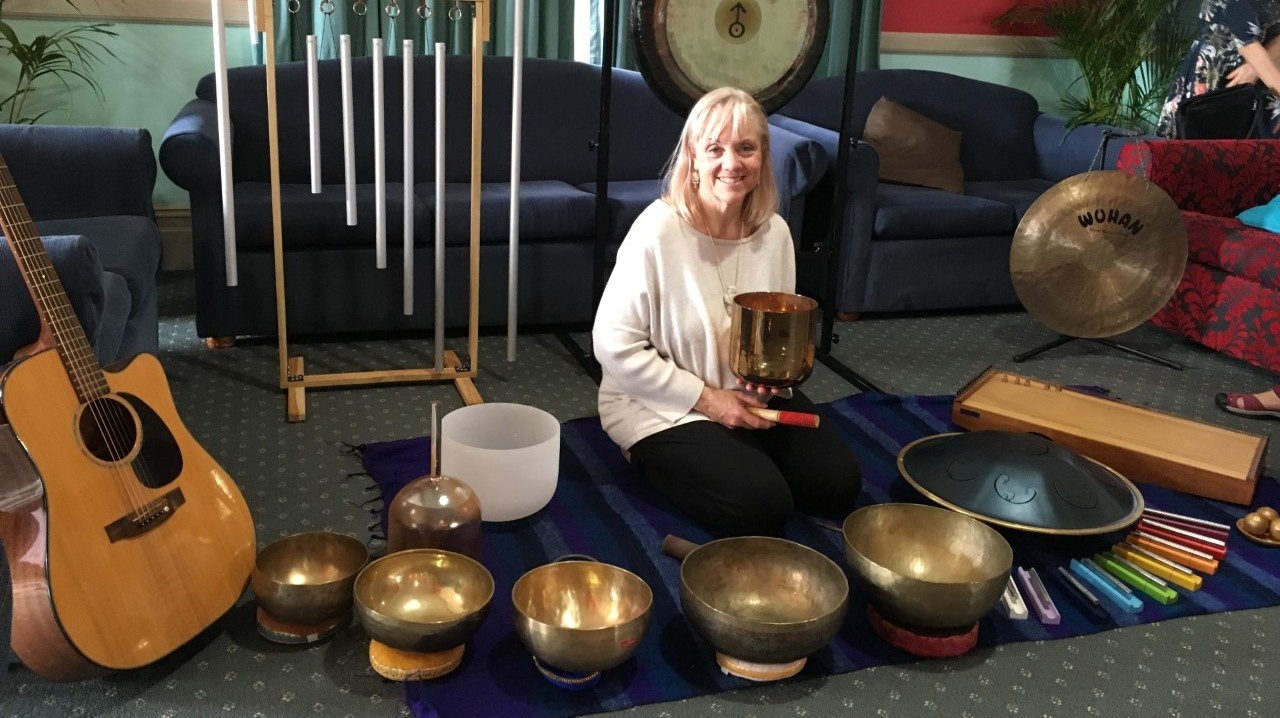 Woman holding a tibetan singing bowl in a room full of sound healing instruments