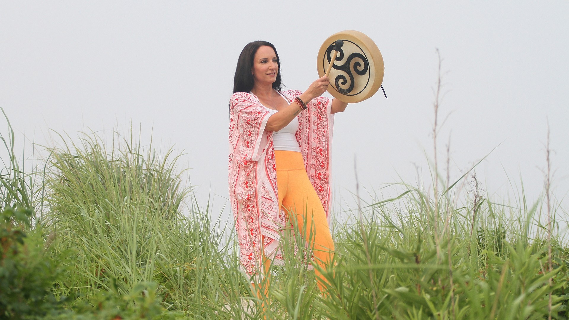 Sound healing practitioner woman drumming in nature in high grass