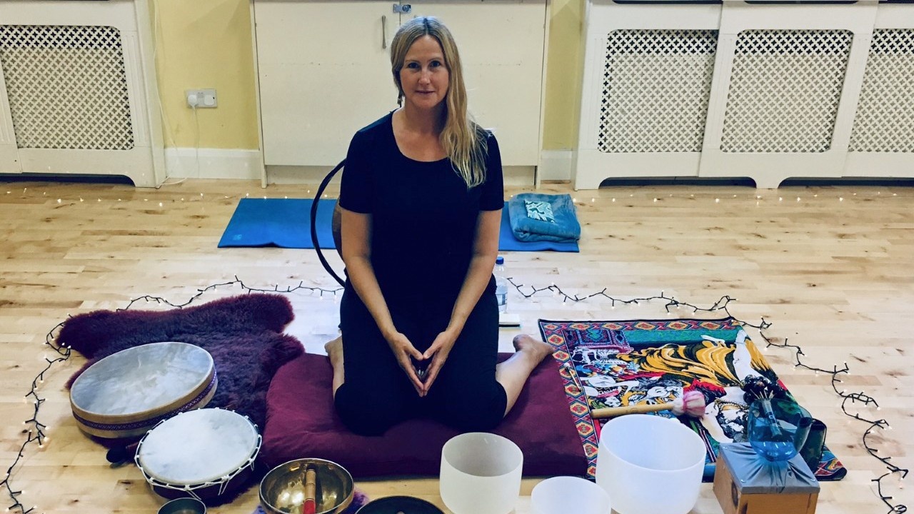Sound healing practitioner surrounded by many sound healing instruments on a wooden floor