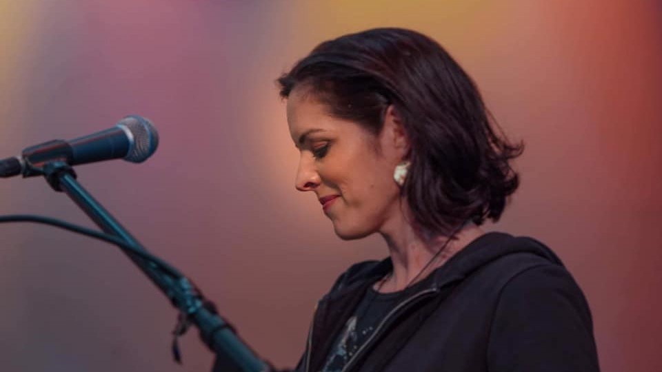 Woman smiling and looking at her microphone, with a coloured background