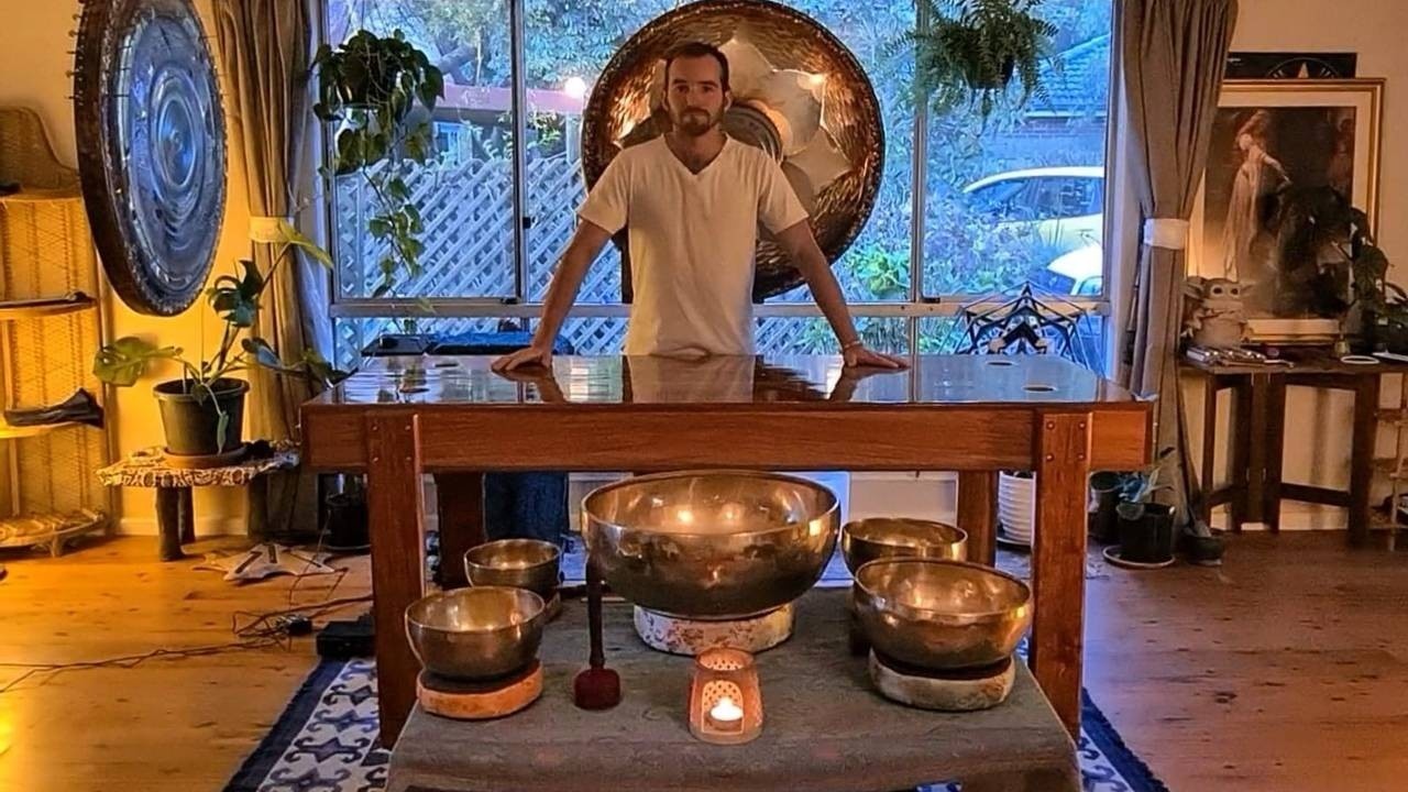 Man with his hands on a healing table, above sound healing instruments in a sound healing room