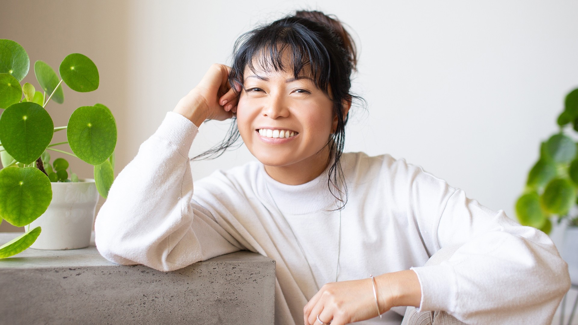 Woman in a white blouse, sitting down next to indoor plants