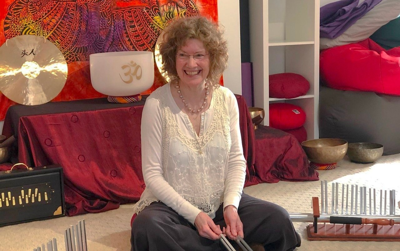 Woman smiling and holding tuning forks in a room with sound healing instruments