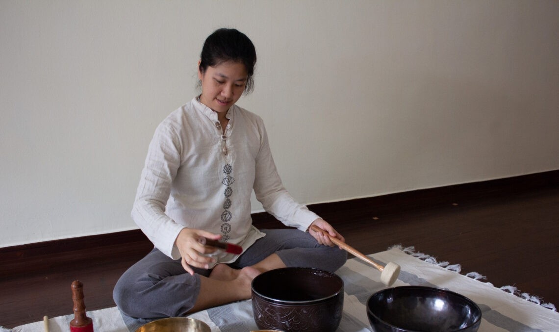 Woman playing a tibetan singing bowl on a white rug indoors