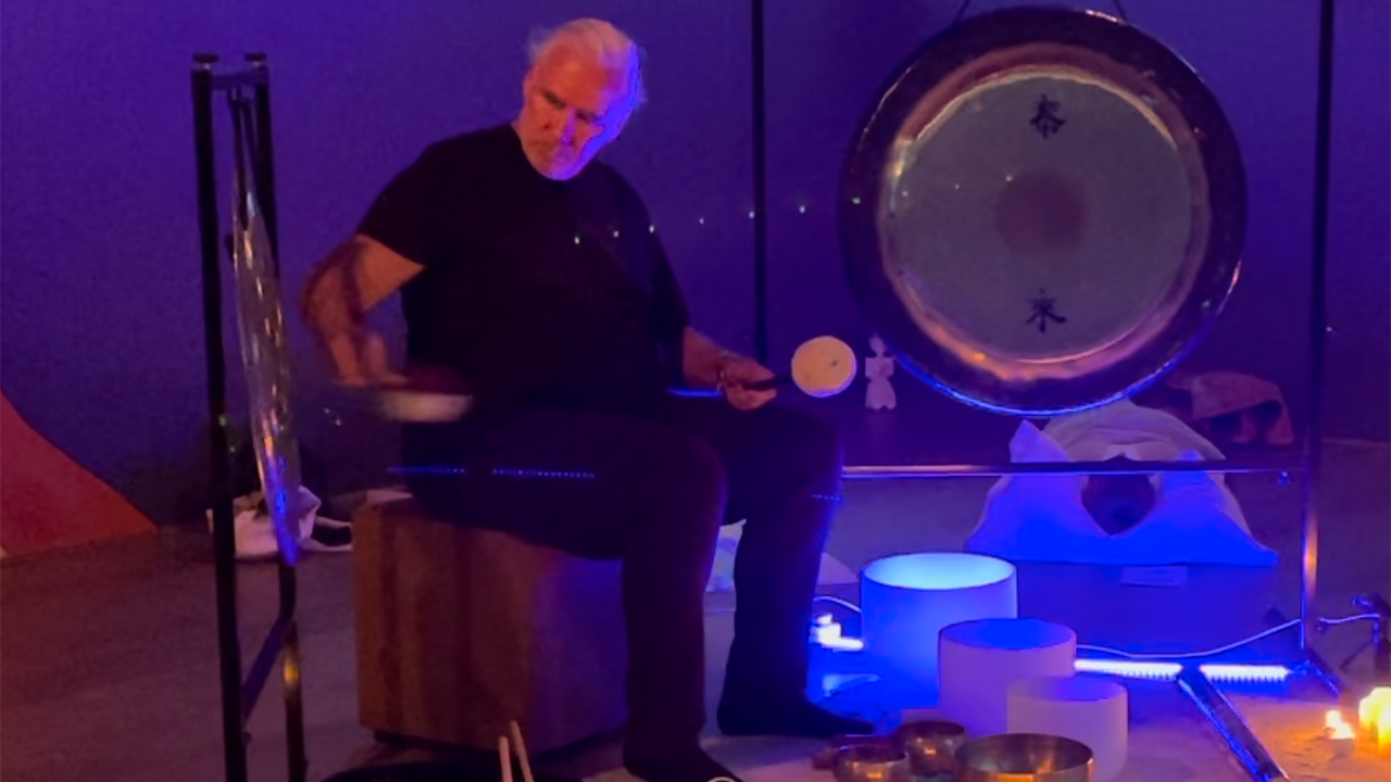 Man playing sound healing instruments in a room with deep blue lightning 
